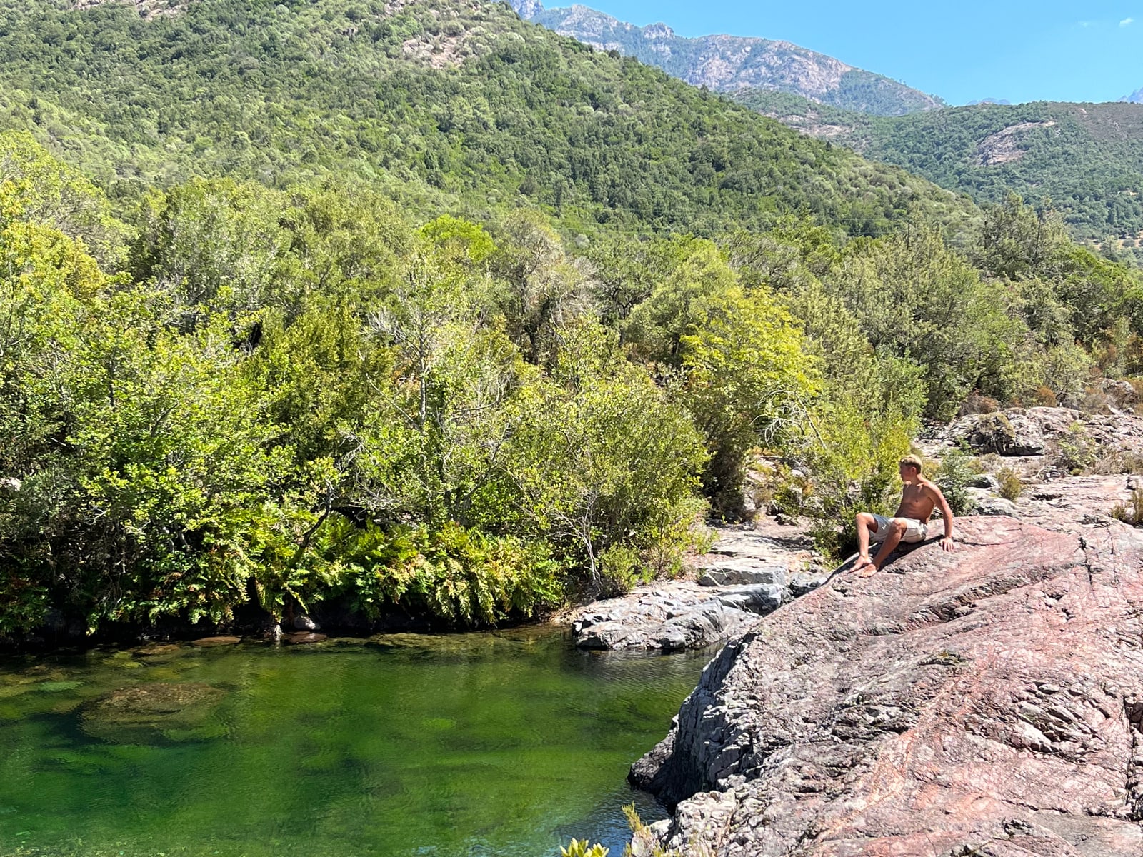 Clear green freshwater pool in the Fango valley with rock slabs and mountains — a person relaxing on the bank