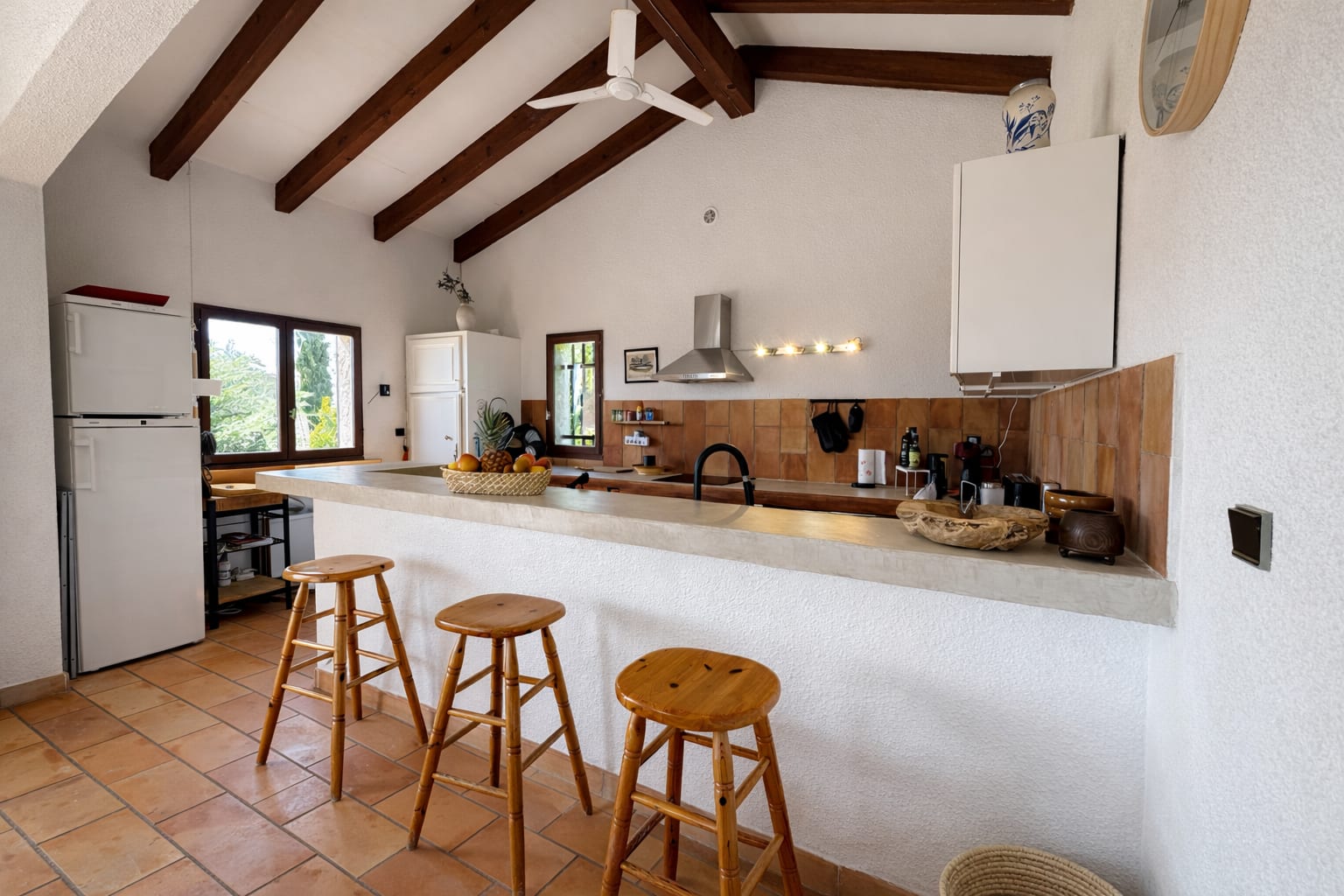 Offene Wohnküche mit Esstresen und drei Holzhockern